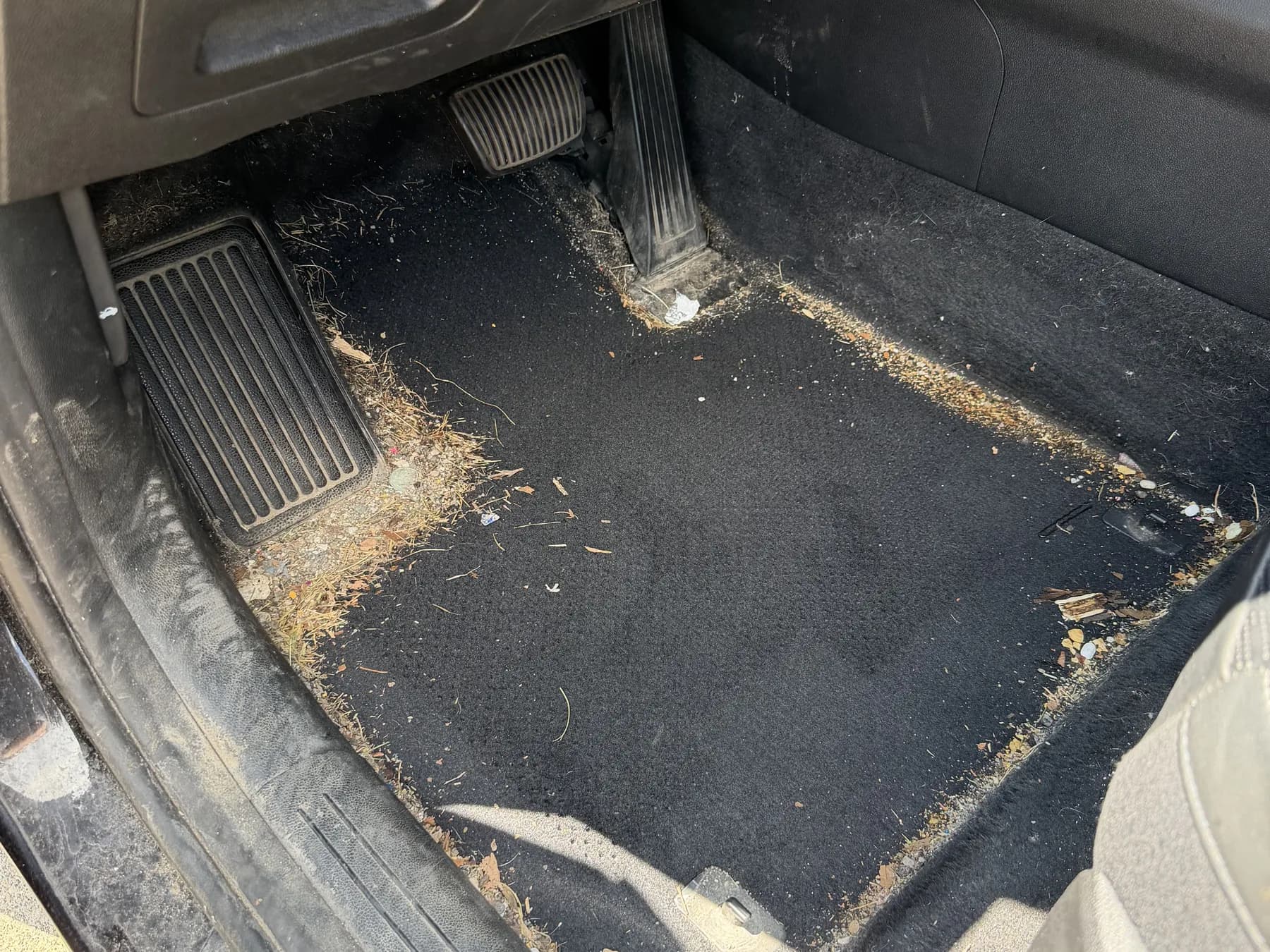 Driver footwell carpet full of dirt and debris before an interior detail at Waterford Auto Shine